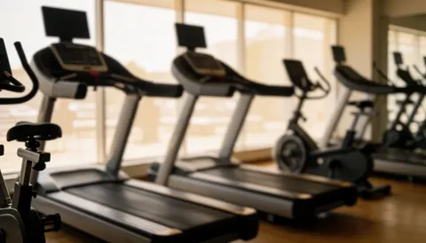 Arrière-plan de salle de sport dédiée au cardio avec tapis de course et vélos d'appartement, éclairage doux et chaleureux, idéal pour des textes promotionnels liés aux cours de boxe.