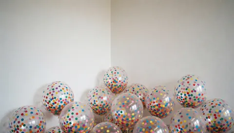 Ballons transparents remplis de confettis multicolores disposés dans un coin d'une pièce blanche, créant une ambiance festive et lumineuse pour la décoration d'événements.