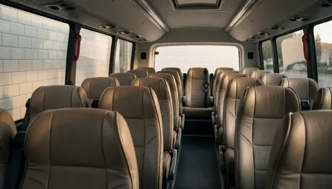 Vue intérieure d'un autobus montrant des sièges en cuir, des murs carrelés blancs et la lumière du coucher de soleil entrant par les fenêtres latérales.