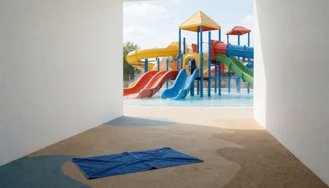 Une serviette bleue sur le sol d'un parc aquatique avec des toboggans colorés et une personne en arrière-plan.