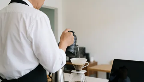 Un barista surveille la préparation du café avec un filtre V60 dans un café propre, dans une ambiance calme et professionnelle.
