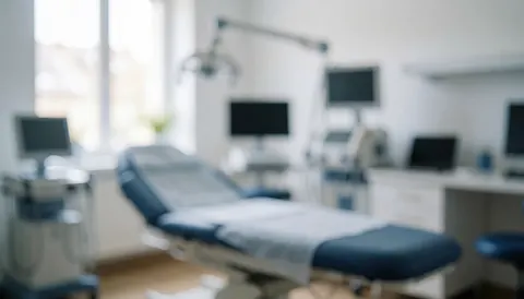 Vue d'un lit de traitement dans une salle médicale avec moniteurs et équipement, offrant un fond neutre adapté aux textes ou logos de services dermatologiques.