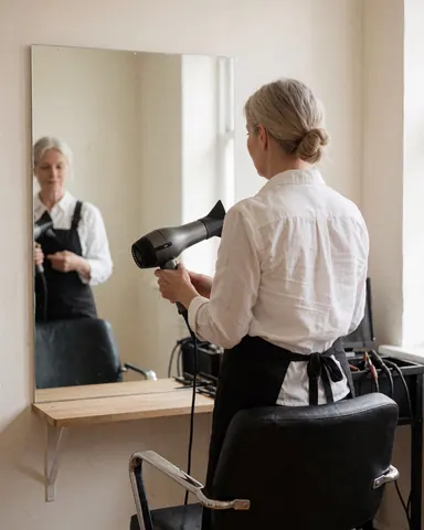 Coiffeur utilisant un sèche-cheveux dans un salon, avec miroir et chaise de coiffure, murs clairs, scène professionnelle et réaliste.