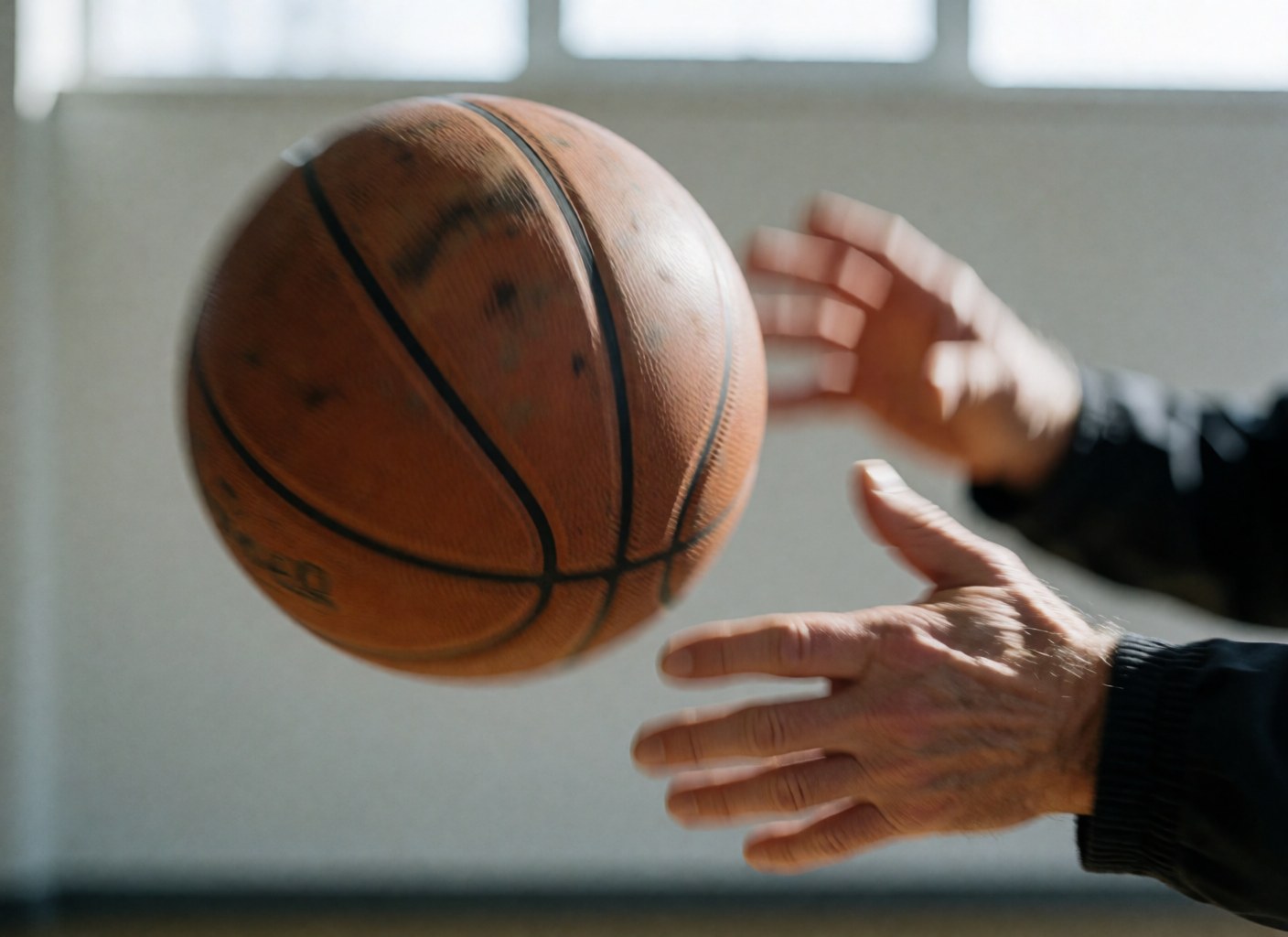 Gros plan d'une main adulte transmettant un ballon de basket dans un gymnase éclairé, mettant en valeur la dynamique et la technique du geste sportif.