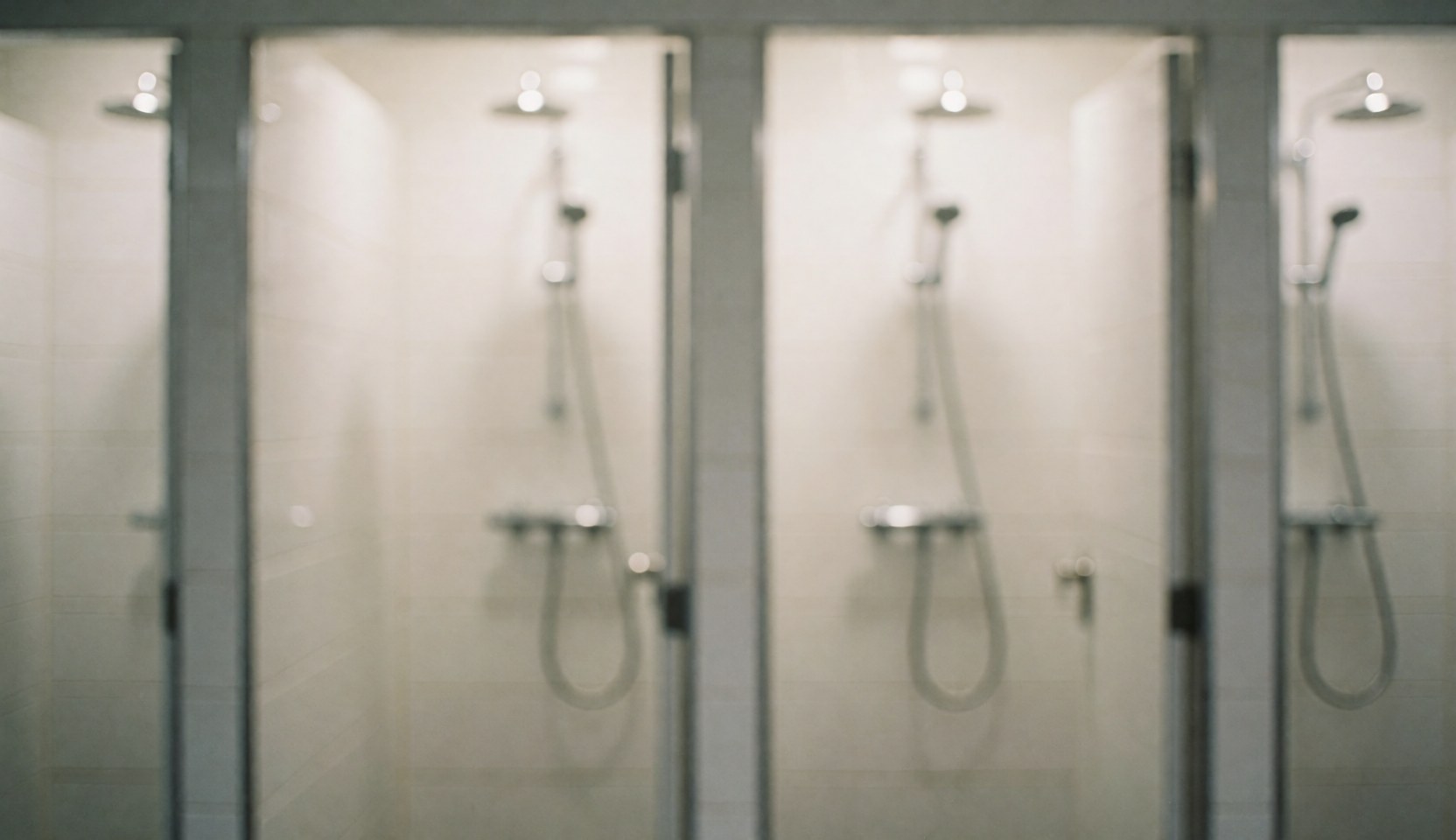 Douches équipées de robinets métalliques dans une salle de bain aux murs carrelés de blanc, offrant un fond neutre et propre adapté aux textes commerciaux.