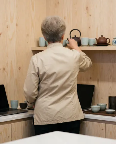 Vue arrière d'un praticien de shiatsu disposant une théière et des tasses dans un local aux murs en bois clair.