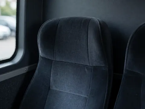 Siège de bus vide en tissu sombre avec coutures apparentes, parois grises et éclairage bleu, idéal pour le transport public.