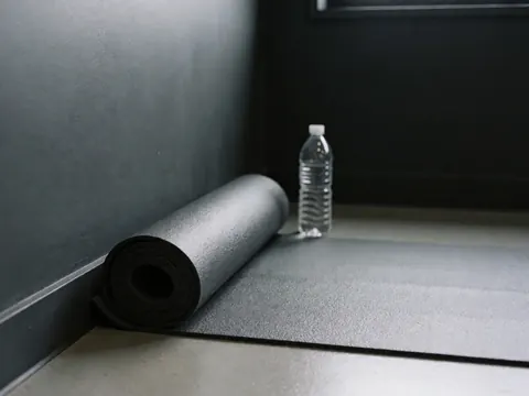 Tapis de yoga enroulé près d'une bouteille d'eau dans un coin de studio de danse aux murs gris anthracite, détail des équipements de classe.
