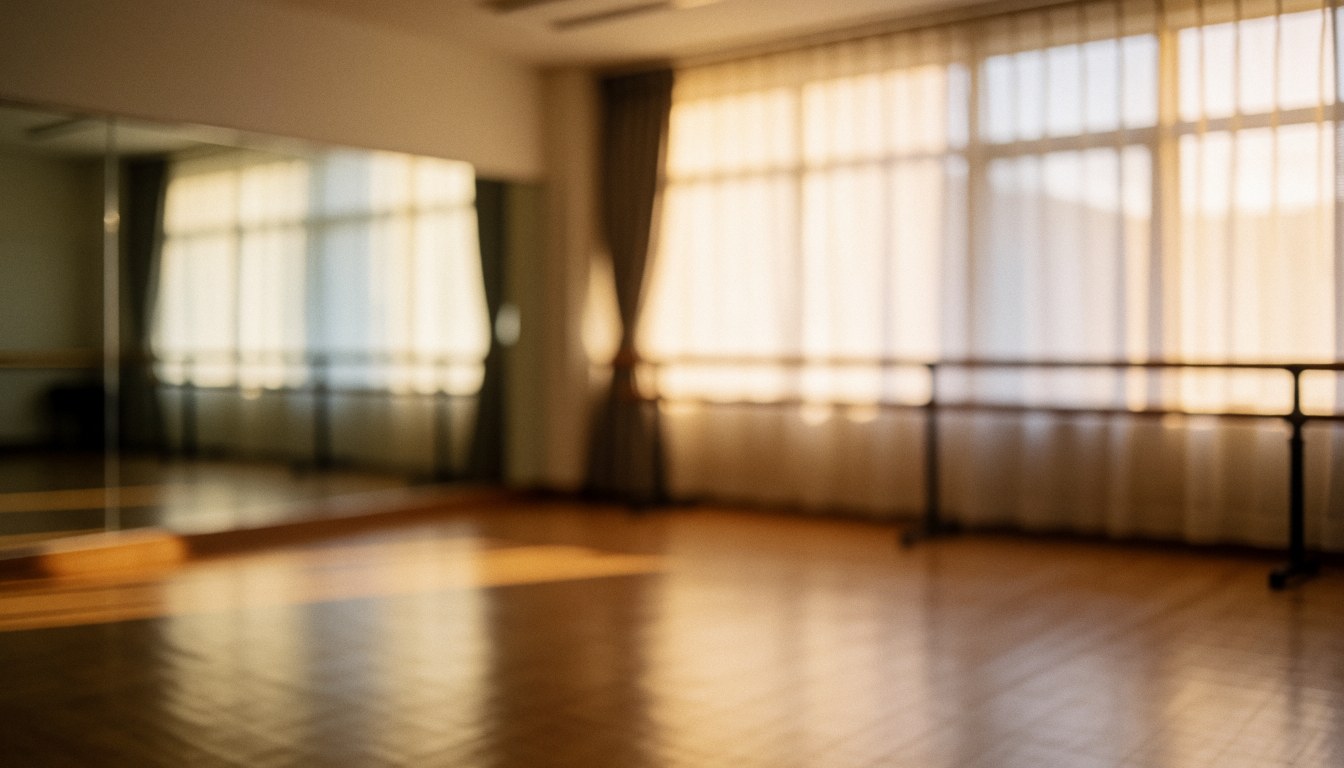 Studio de danse vide avec sol en bois, miroirs et barre de ballet, éclairé par une lumière chaude provenant de fenêtres avec rideaux.