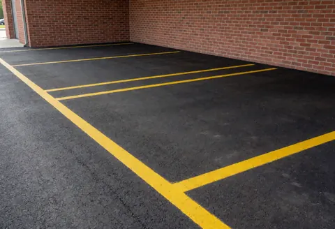 Vue d'un stationnement avec des lignes de marquage jaunes sur l'asphalte et un mur de briques rouges en arrière-plan, prêt à accueillir des véhicules.