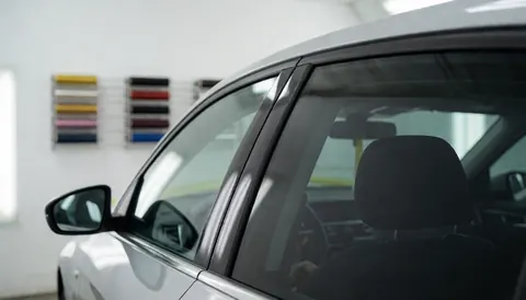 Voiture équipée de vitres teintées dans un atelier de vitrerie, avec des échantillons de film en arrière-plan sur des murs blancs.