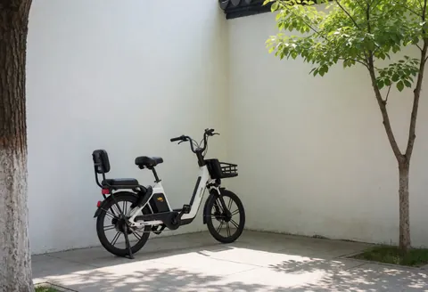 Un vélo électrique avec siège arrière est garé sur une place pavée entourée de murs blancs et d'ombres d'arbres, adapté au transport écologique en zone touristique.