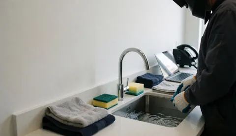 Une personne avec des gants nettoie un évier à l'aide d'éponges et de serviettes, illustrant les soins apportés au matériel de photographie sous-marine.