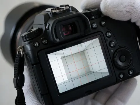 Appareil photo professionnel affichant une grille de nivellement sur son écran lcd. Une main gantée ajuste un cadran. Fond en béton lisse. Détail technique pour photographes panoramiques.