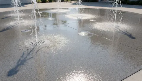 Fond de parc aquatique avec des jets d'eau projetés sur un sol en béton humide et des grilles d'évacuation circulaires, idéal pour une bannière de site web.