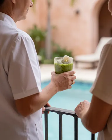 Une cliente en uniforme blanc profite d'un plat d'aguachile au bord de la piscine d'un resort, avec un fond flou et une lumière naturelle.