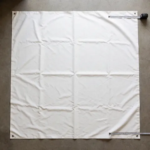 Tissu blanc de store avec crochets métalliques aux coins, sur sol en béton, avec mètre ruban pour mesurer, idéal pour l'installation de stores.