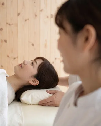 Un thérapeute applique un massage cervical profond sur un client allongé sur une table de massage dans un cadre professionnel avec des murs en bois clair.