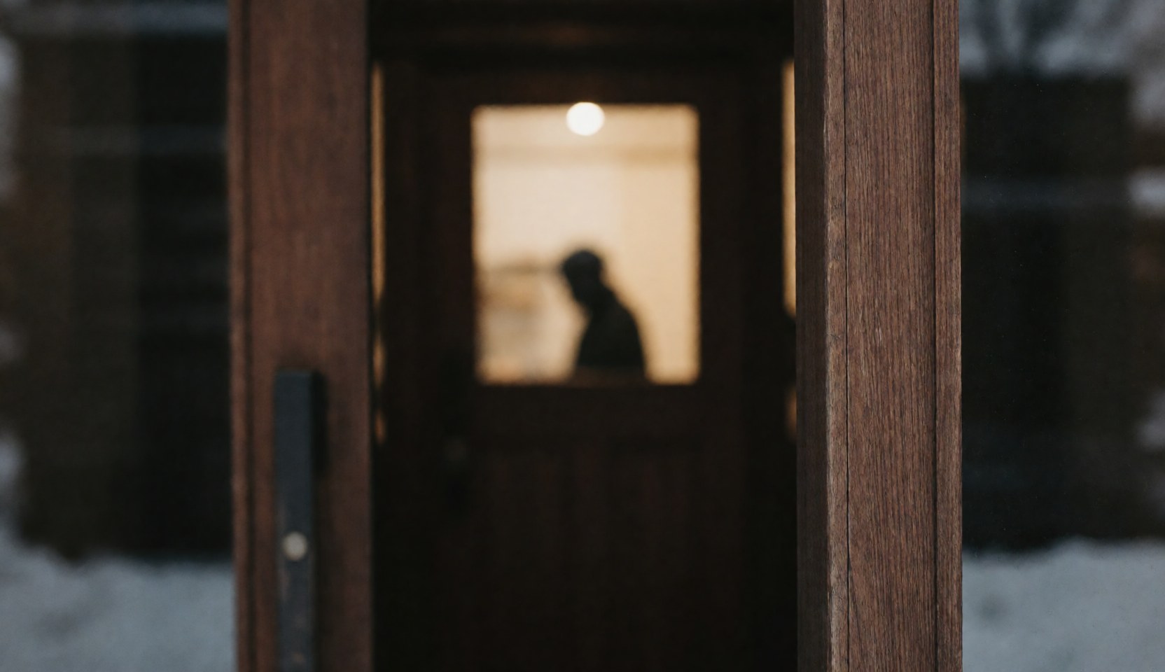 Porte en bois sombre éclairée par une lumière chaude à l'intérieur, avec de la neige à l'extérieur, idéale pour un fond de texte dans un refuge de montagne.