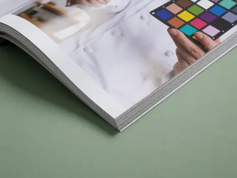 Magazine ouvert montrant une carte de contrôle des couleurs sur une surface brillante avec un fond vert, outil utile pour la photographie de produits et la précision des couleurs.