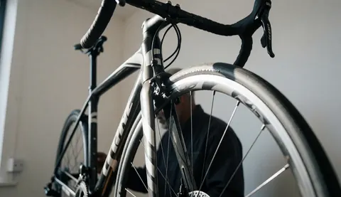 Détail d'un vélo de route avec cadre en carbone dans un atelier de réparation, avec une personne travaillant en arrière-plan.