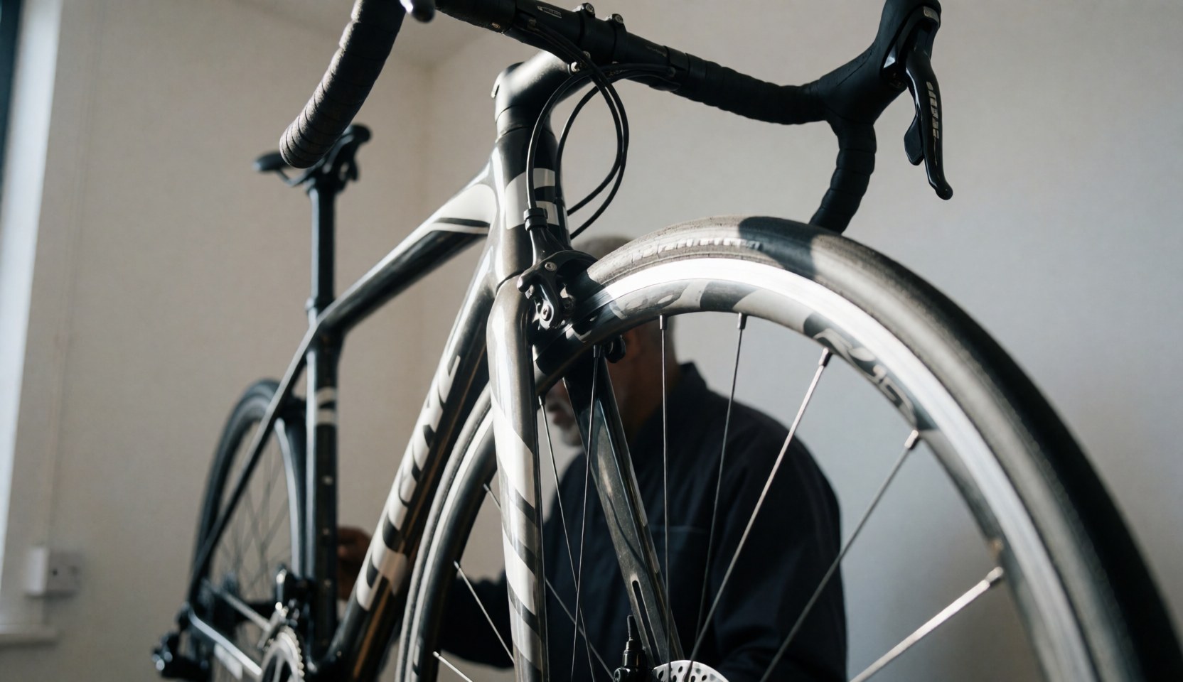 Détail d'un vélo de route avec cadre en carbone dans un atelier de réparation, avec une personne travaillant en arrière-plan.