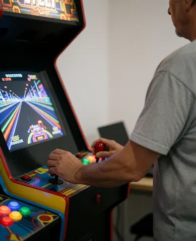 Un adulte joue à un jeu de course sur un borne d'arcade avec des boutons colorés et un écran lumineux.