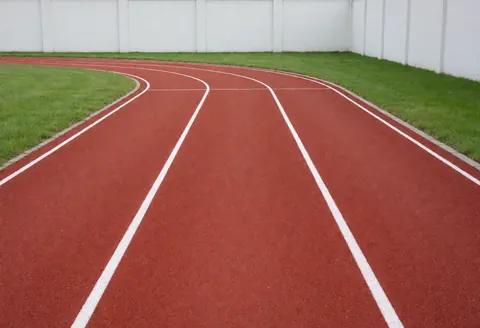 Piste d'athlétisme vide avec lignes blanches, pelouse verte et murs blancs, idéale pour l'entraînement.
