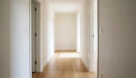 Couloir vide aux murs blancs et au sol en bois, éclairé par une lumière naturelle en bout de corridor, offrant un fond neutre adapté à l'ajout de textes commerciaux.