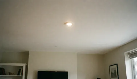 Plafonnier LED encastré dans un plafond blanc avec des murs lisses et propres, offrant un fond neutre et professionnel pour des textes sur les services électriques résidentiels.