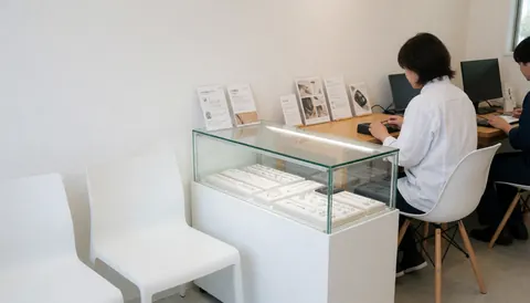 Vitrine en verre exposant des bijoux dans un studio de piercing moderne avec des chaises blanches et du personnel travaillant sur des ordinateurs.