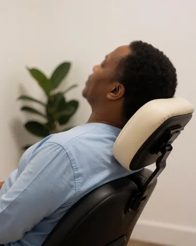 Client profitant d'un massage en fauteuil avec une plante en arrière-plan, mur blanc et lumière chaude pour promouvoir les services de massage.