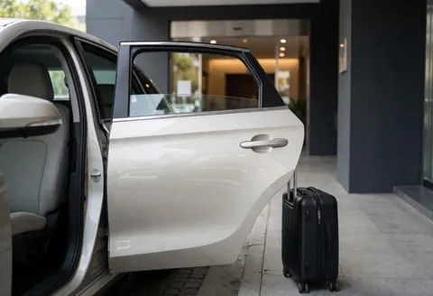 Véhicule de transport moderne avec porte ouverte et valise noire à l'extérieur d'un hôtel, prêt à accueillir un client.