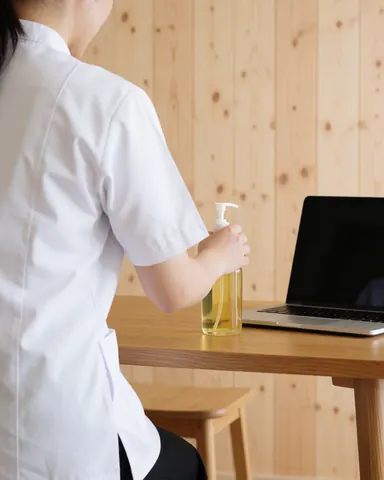 Un thérapeute en uniforme blanc prépare de l'huile de massage sur une table en bois dans un centre de soins.