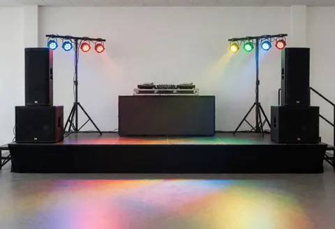 Scène de fête vide équipée de tables de DJ, d'enceintes et de lumières colorées prêtes pour l'événement.