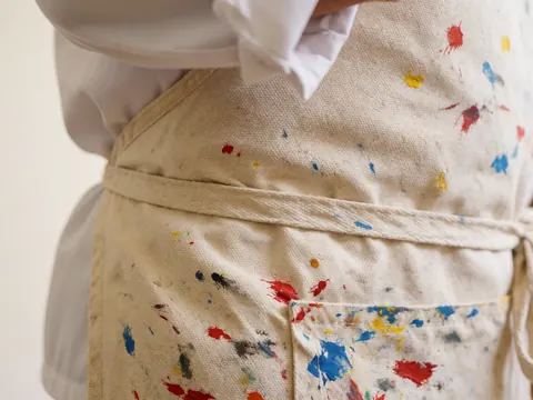 Ceinture de tablier en toile avec des taches de peinture rouge, bleue et jaune, détail d'outils artistiques dans un studio de peinture.