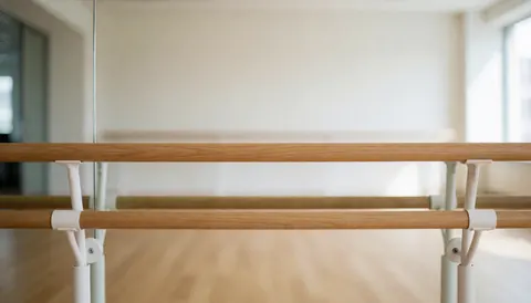 Barre de ballet en bois clair installée dans un studio de danse avec des miroirs et un sol lumineux, offrant un fond professionnel adapté à l'ajout de textes.