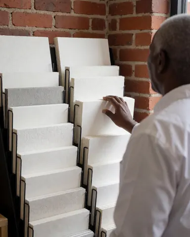 Une cliente examine une variété de papiers texturés sur une étagère dans un magasin de papeterie avec un mur en briques rouges.