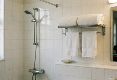 Salle de bain d'hôtel avec carreaux blancs, douche chromée, serviettes blanches sur porte-serviettes et savon sur plat, idéale pour l'hébergement.