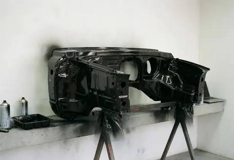 Châssis de carrosserie automobile peint en noir brillant sur support métallique en atelier, accompagné de sprays et d'une palette de peinture.