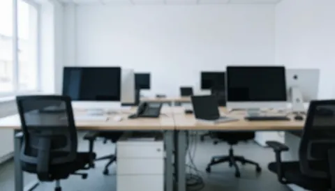 Espace de travail moderne et épuré, équipé de tables blanches, de chaises de bureau et d'ordinateurs, offrant un fond neutre idéal pour l'ajout de texte.