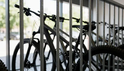 Fond industriel montrant des vélos de montagne stationnés derrière des grilles métalliques, adapté comme arrière-plan textuel pour un service de coaching en cyclisme.
