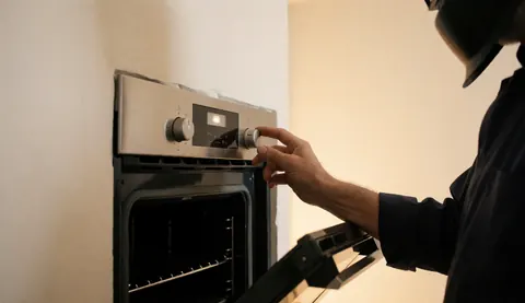 Technicien en train de régler le thermostat d'un four avec le panneau de contrôle ouvert, dans un environnement propre et bien éclairé, illustrant une intervention de maintenance professionnelle.