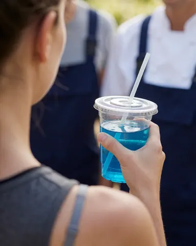 Client tenant un gobelet avec une boisson bleue dans un parc d'aventure, avec des employés en arrière-plan portant des tenues de travail.