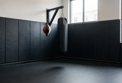 Coin dédié à la boxe avec sac de frappe et speed bag, murs rembourrés et sol en caoutchouc, idéal pour l'entraînement en salle de sport.