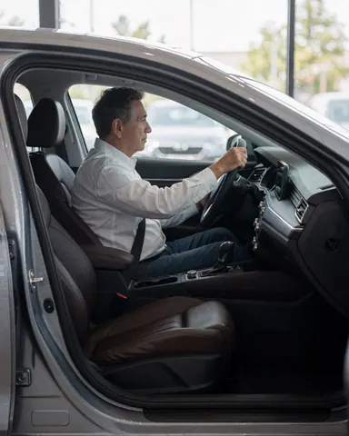 Vue extérieure d'un client assis à l'intérieur d'un sedan avec des sièges en cuir dans un concessionnaire automobile.