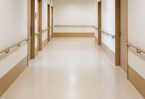 Couloir large et accessible doté de barres d'appui en bois, de sol lisse et de murs blancs, adapté aux centres de soins.