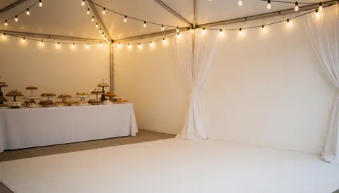 Tente blanche ornée de guirlandes lumineuses avec une table à friandises en arrière-plan, idéale pour la coordination d'événements festifs