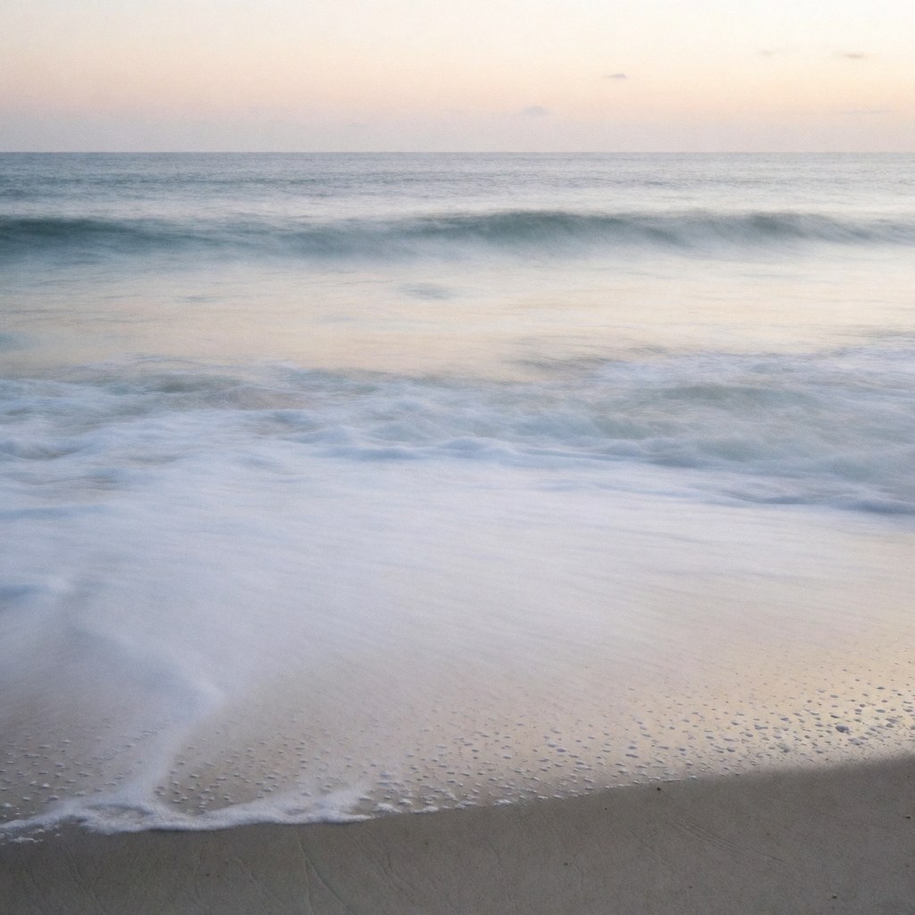 Plage de Copacabana avec des vagues transformées en brume par une longue exposition, sable sombre et ciel doux au coucher du soleil, idéal pour un photographe cinétique.