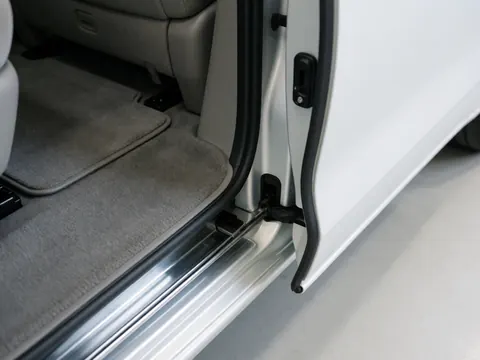 Vue rapprochée de la porte coulissante d'une minivan dans un atelier, révélant le sol en moquette grise et le cadre métallique brillant.